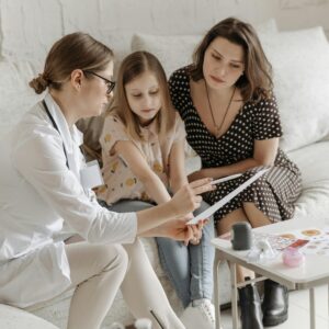 Eine Kinderärztin zeigt einer Mutter und Ihrer kleinen Tochter Informationen auf einem Blatt Papier.