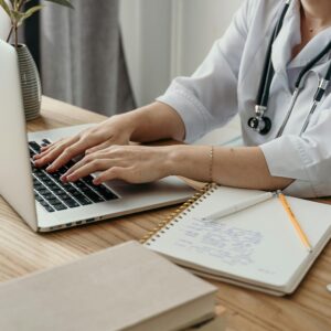 Eine Kinderärztin arbeitet am Laptop, daneben liegt ein Block mit handschriftlichen Notizen.